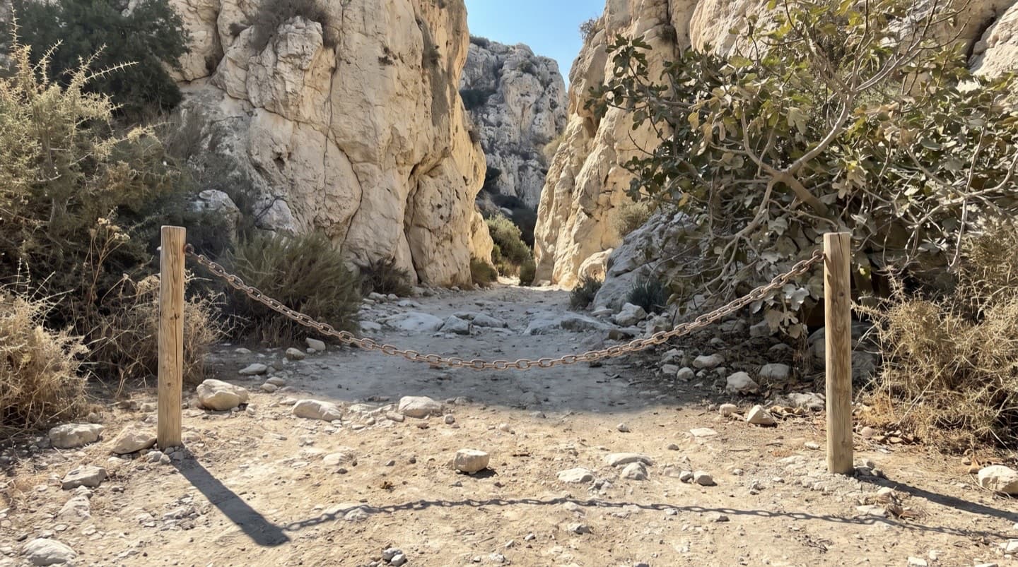 Eine Kette zwischen zwei Pfosten quer über dem Eingang eines steinigen Pfades am Ausgang einer Kalksteinschlucht