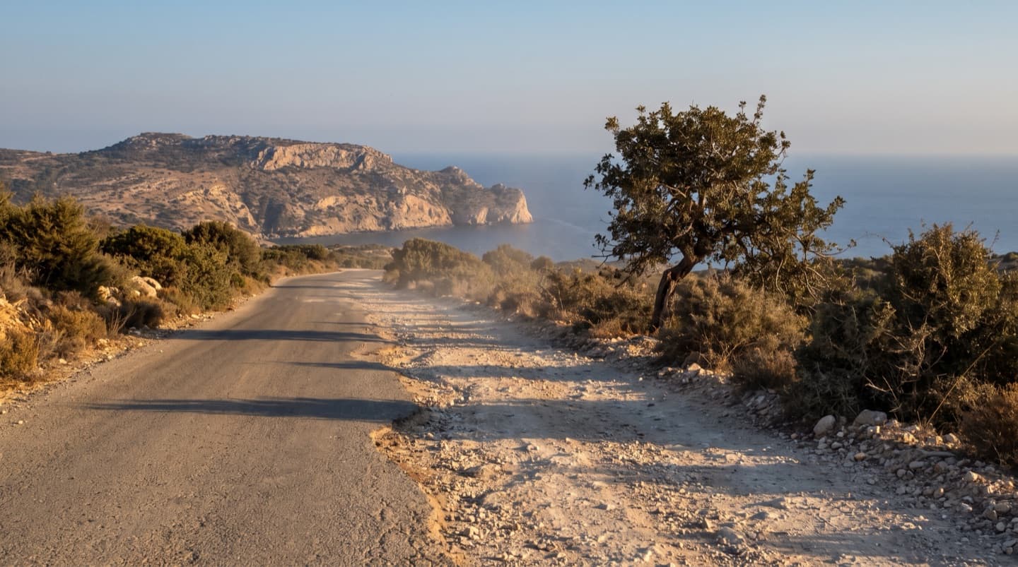 Das Ende eines Asphaltstreifens, der in eine ausgefahrene Stein- und Schotterpiste übergeht, die auf eine Kalksteinlandzunge und das Meer zuläuft
