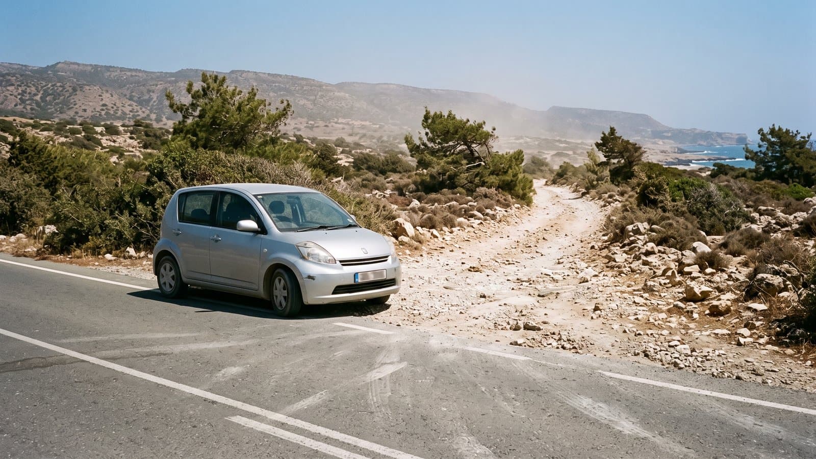 A small hatchback stopped at the exact edge of the tarmac, where the road becomes a rutted stone track running towards a rocky coast