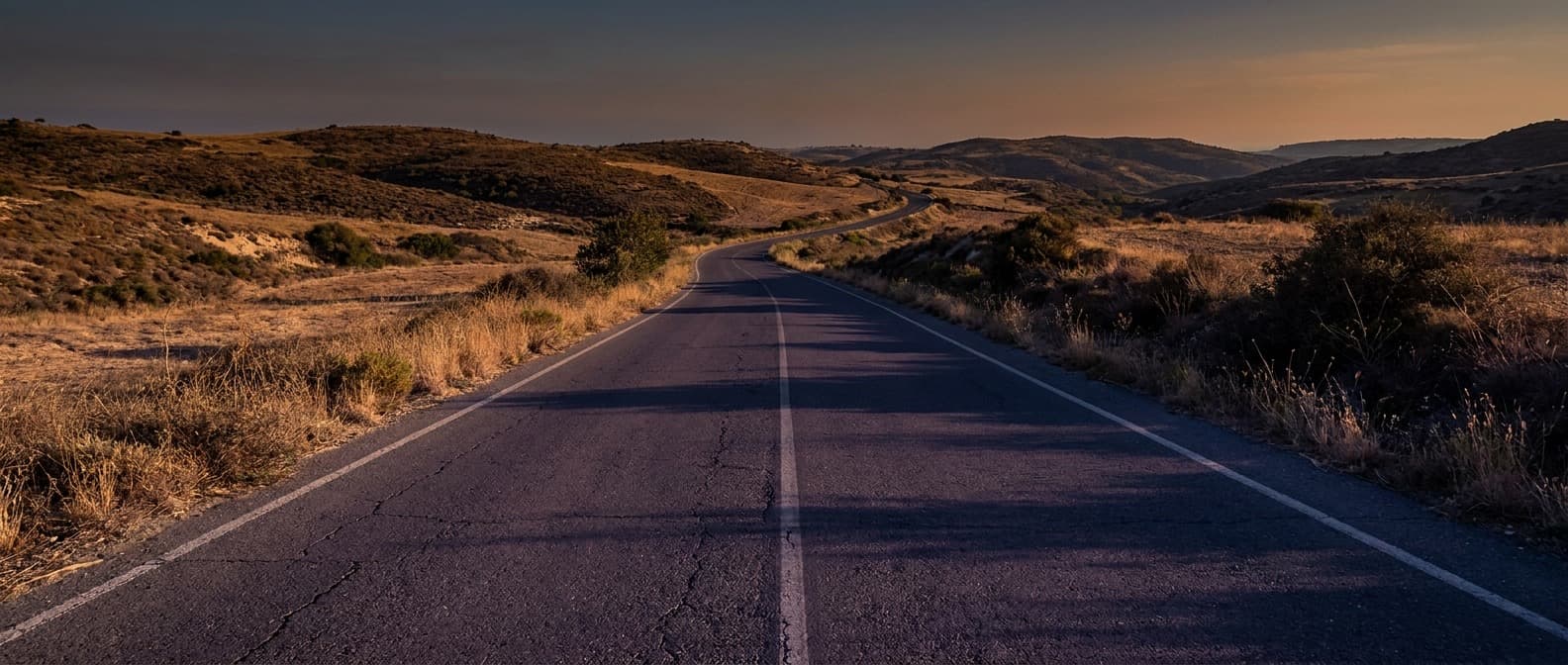 Empty two-lane road crossing dry hills in Cyprus at dusk, the kind of route a hire car covers
